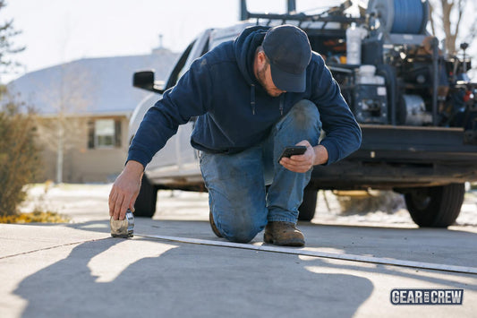 Contractor measuring a residential driveway with a tape measure while working out a quote on his phone
