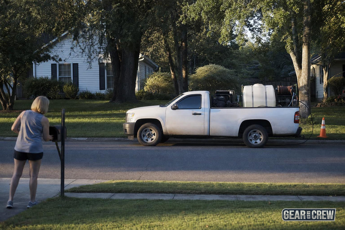 Work truck with pressure washing equipment parked on a quiet suburban street as a neighbor collects mail