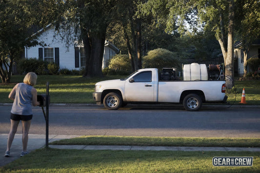 Work truck with pressure washing equipment parked on a quiet suburban street as a neighbor collects mail